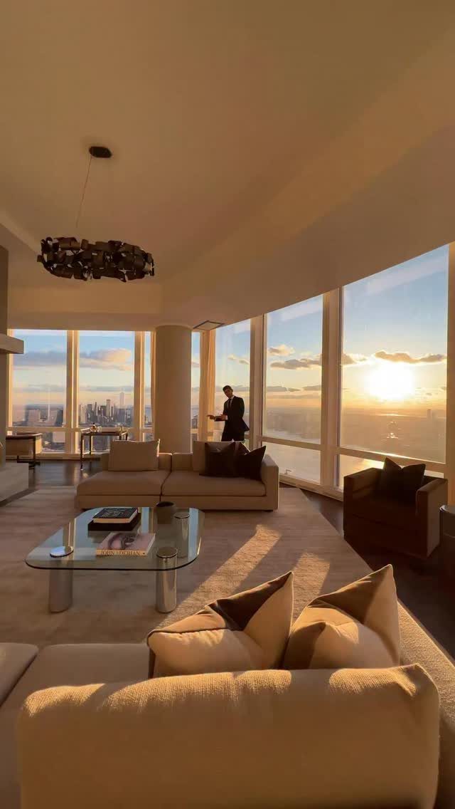 Modern high-rise apartment interior with large windows overlooking a city skyline at sunset.
