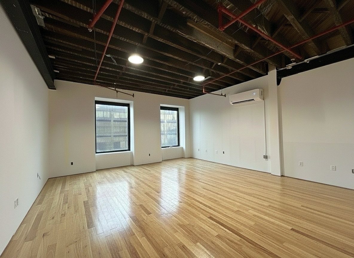 Empty industrial loft with polished wood floors and exposed ceiling beams and pipes.