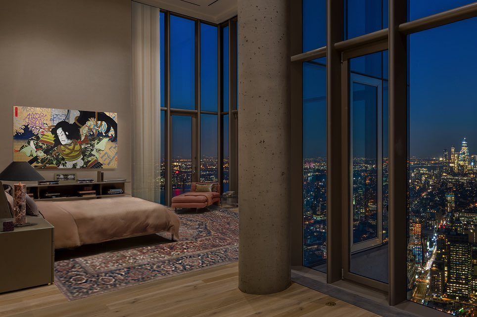 Luxury bedroom with high ceilings and floor-to-ceiling windows overlooking a city skyline.