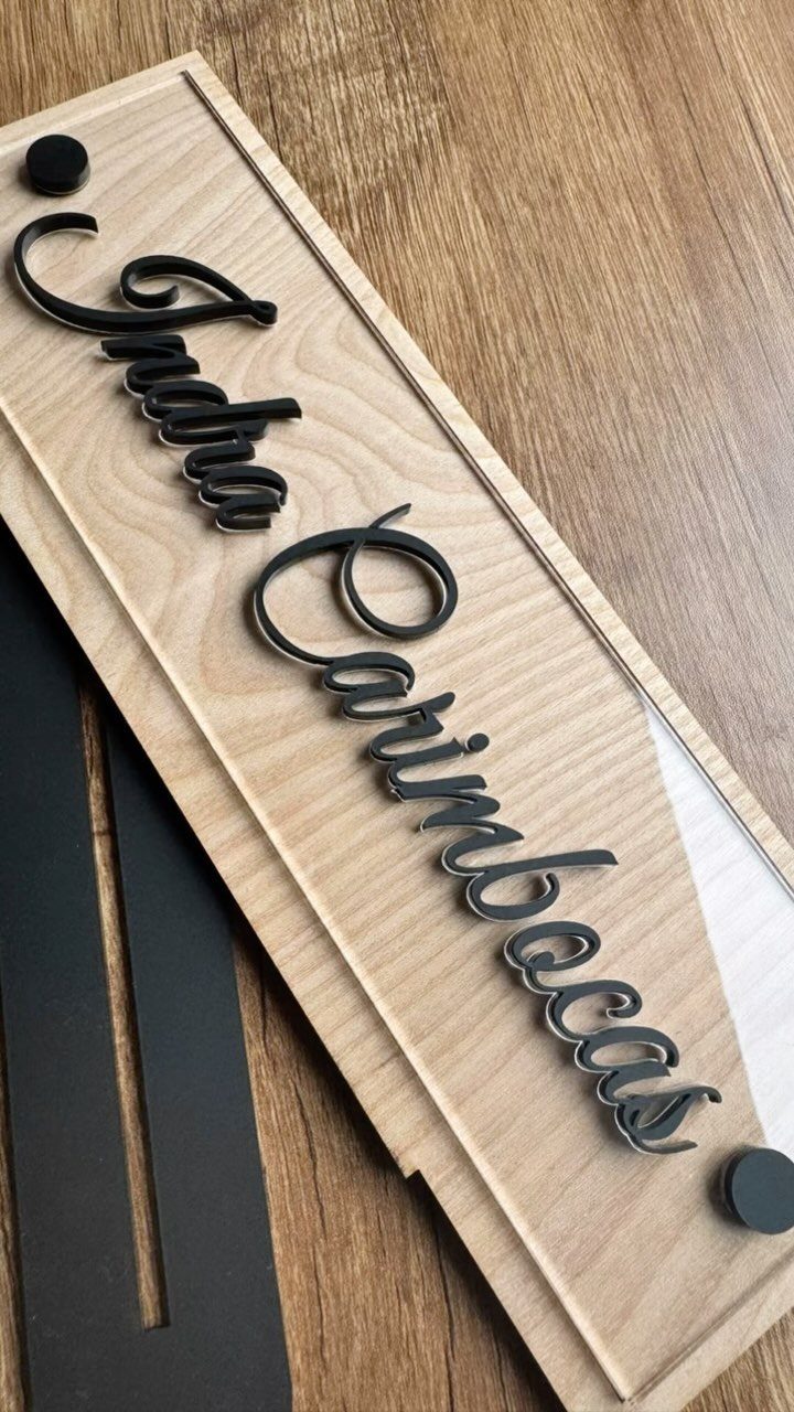 Wooden nameplate with black cursive 3D lettering resting on a wooden surface.