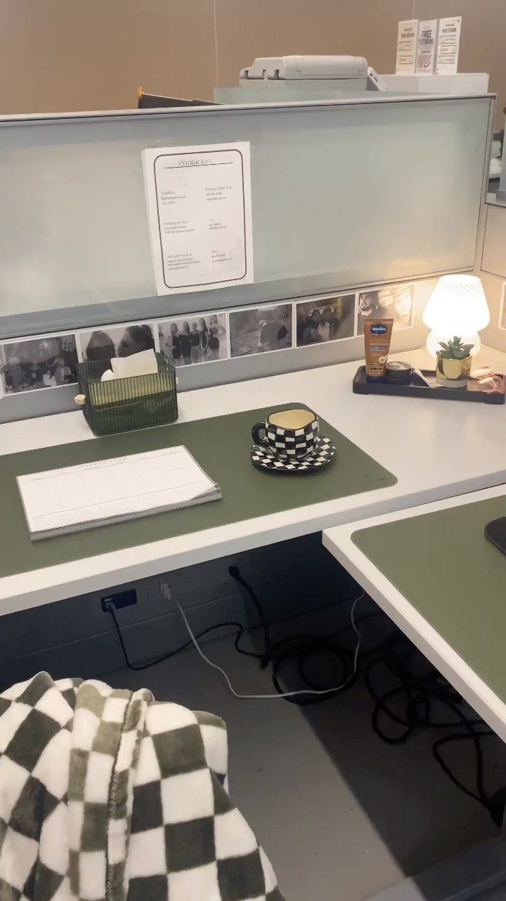 Decorated office cubicle desk with green accents, a small lamp, and personal photos.