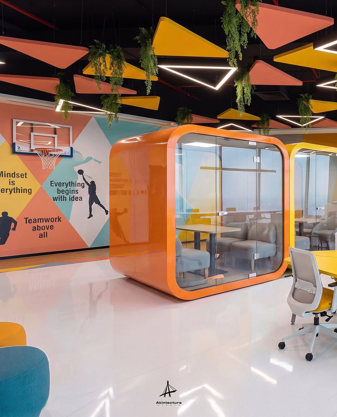 Modern office interior with orange meeting pod, colorful walls, and hanging ceiling plants.