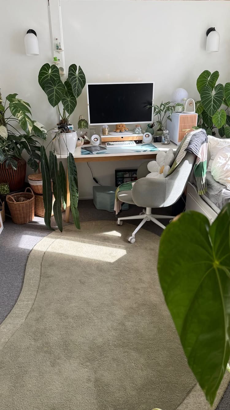 Home office workspace with a white desk surrounded by various lush green indoor plants.