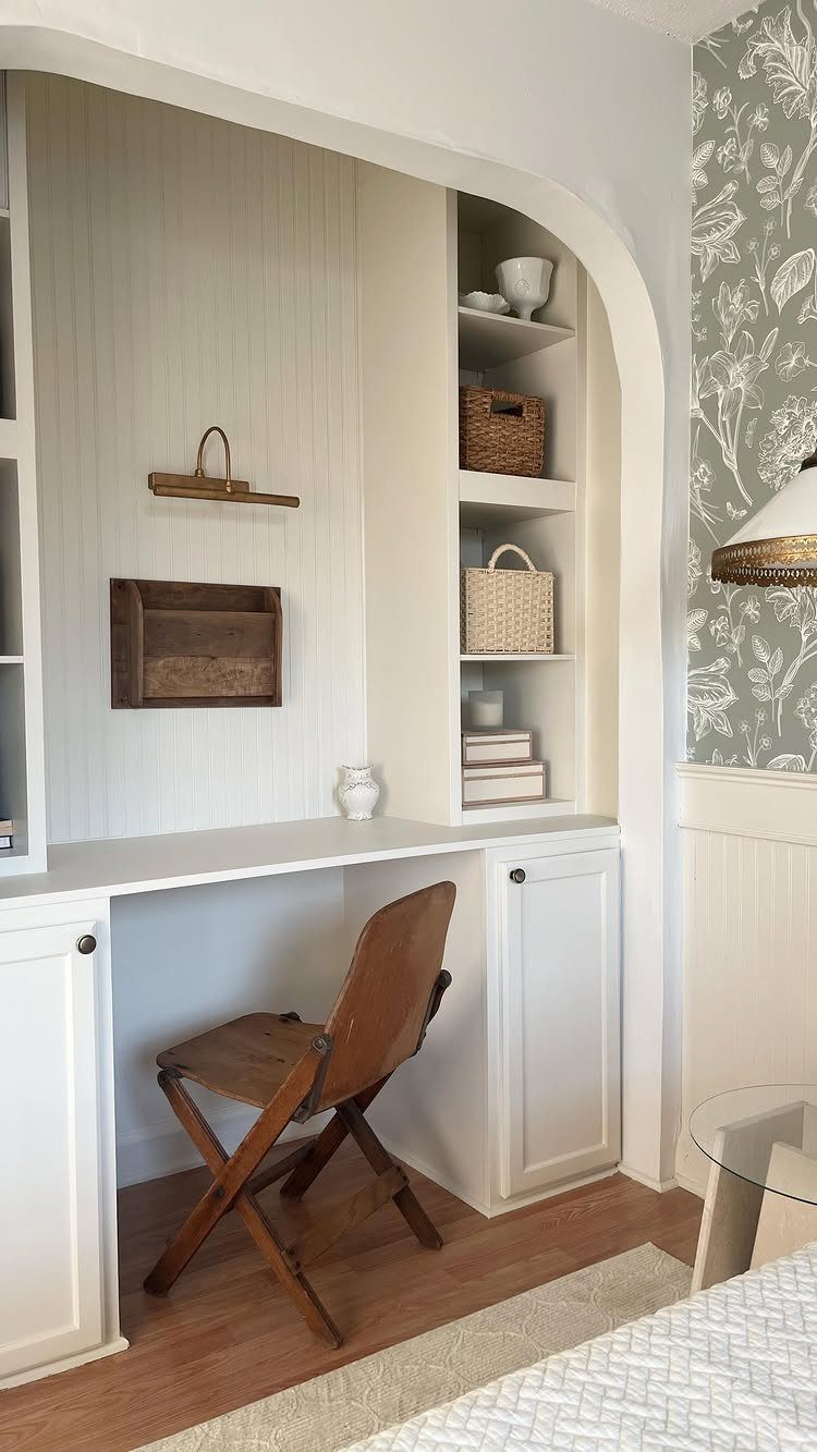 Built-in white desk in an arched alcove with shelving and folding wooden chair