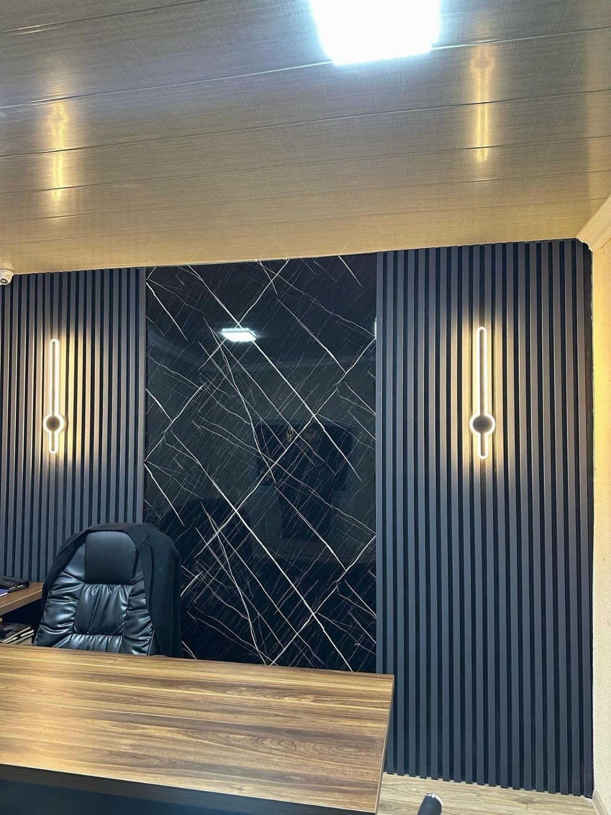 Black slatted office wall with a central marble panel and vertical linear lighting.