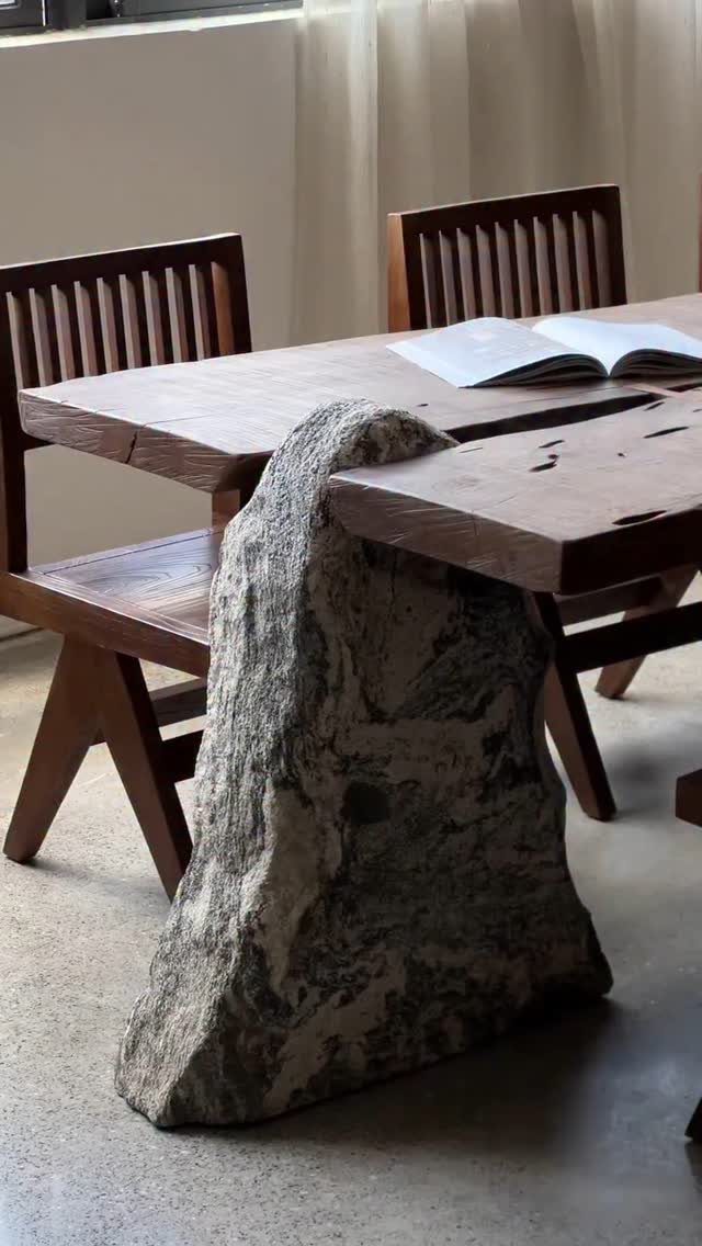 Wooden dining table with a live edge and a large natural stone base.