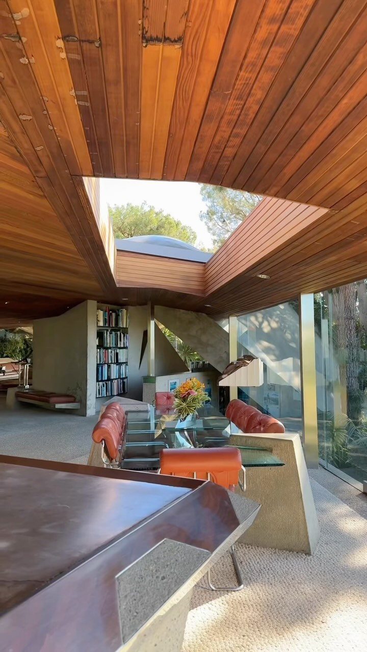 Mid-century modern room with wood paneled ceiling, concrete walls, and orange leather chairs.
