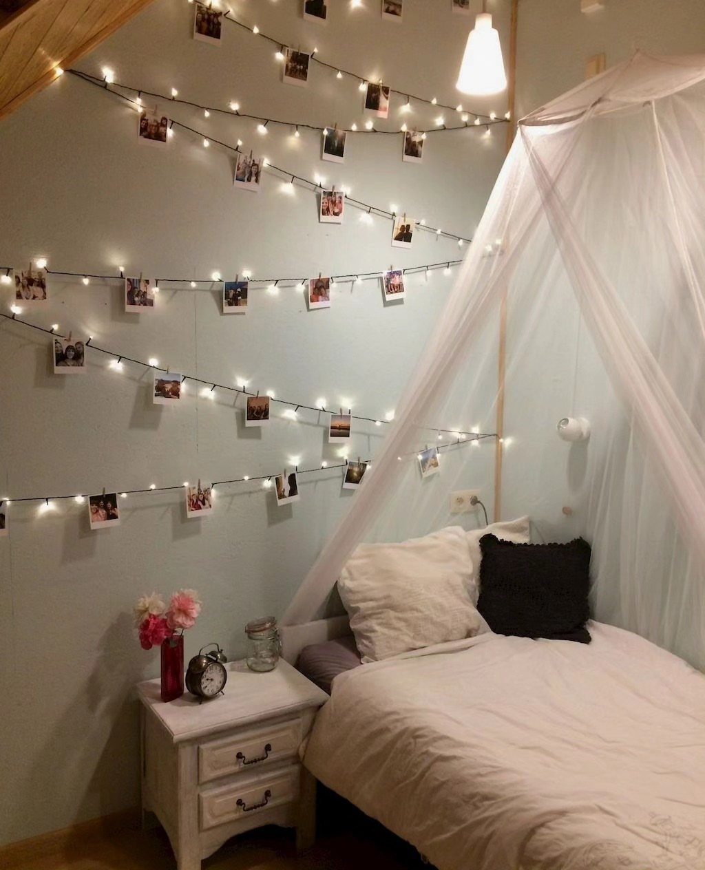 Fairy lights with clipped photos draped across a wall above a canopy bed.