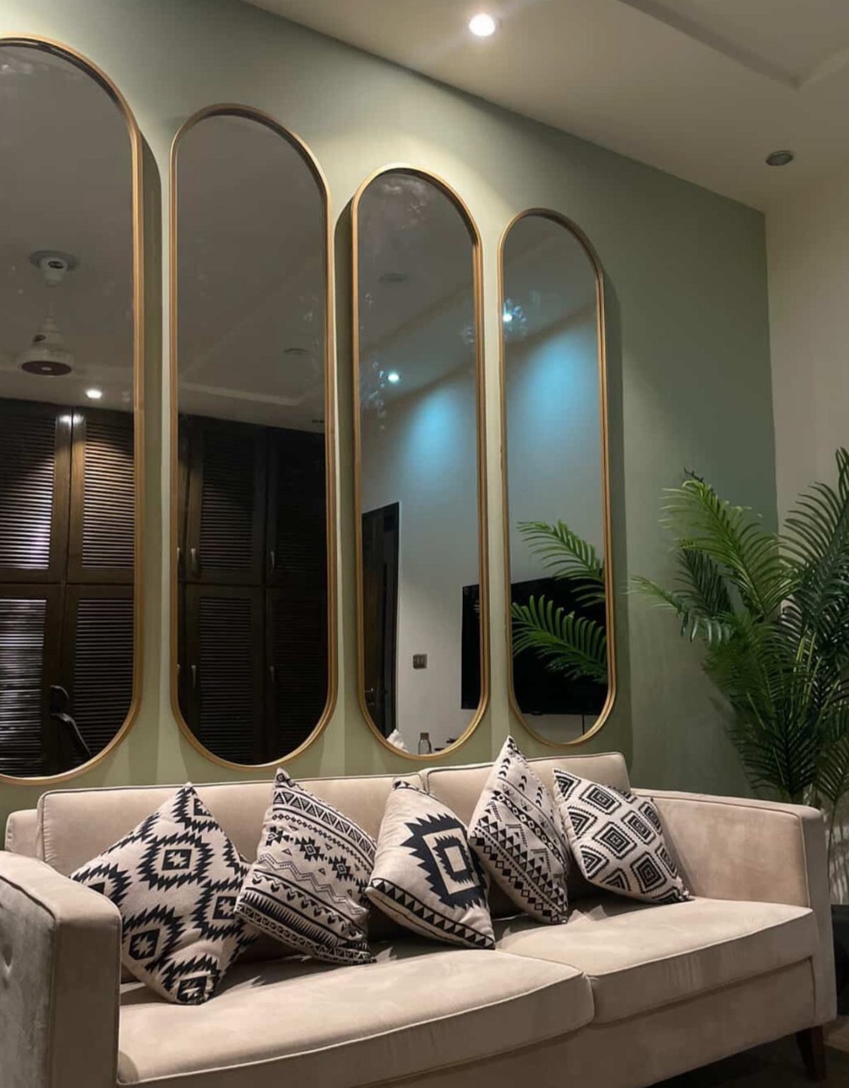 Four arched gold-framed mirrors hanging on a green wall above a beige sofa.