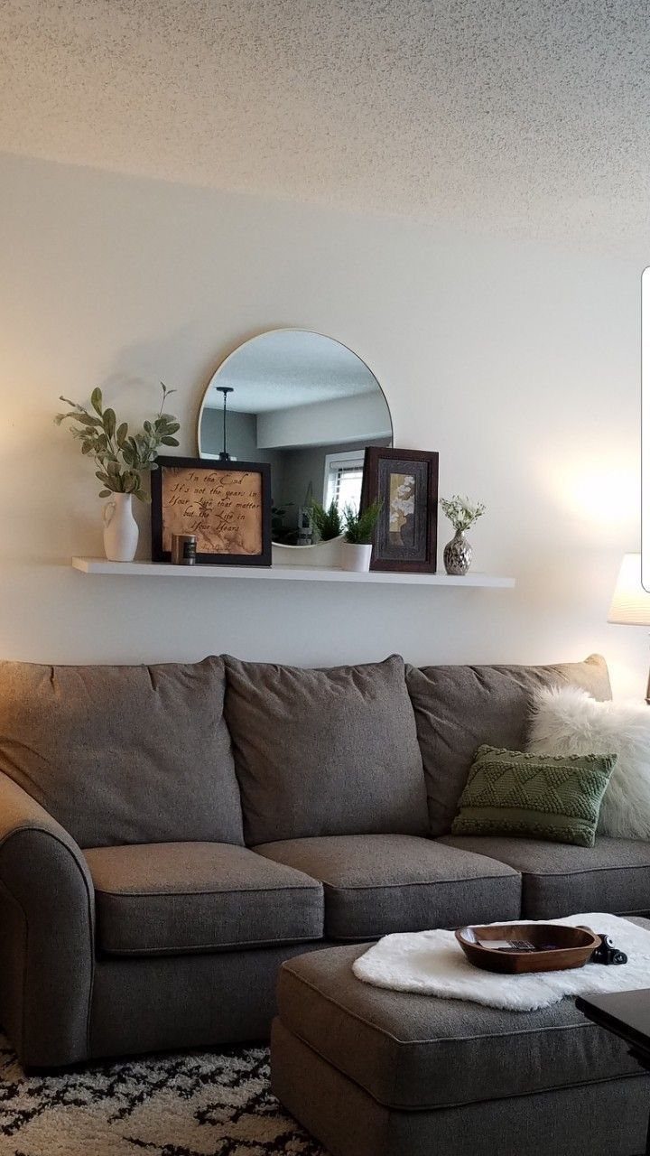 Grey couch with a white floating shelf holding a semi-circular mirror and decor.
