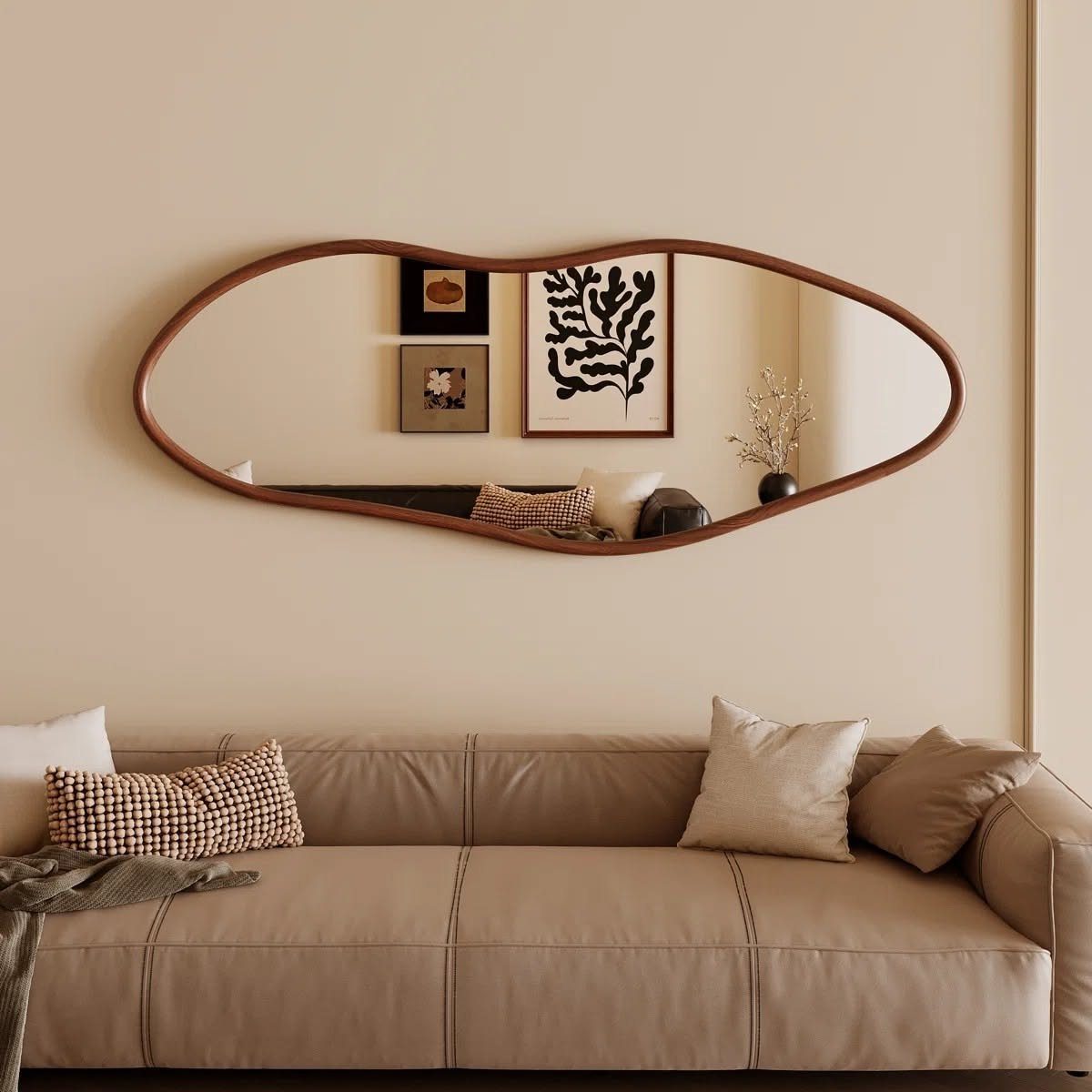 Organic shaped brown framed mirror hanging above a tan leather living room sofa