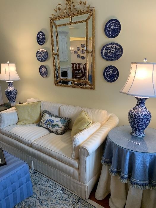 Gold ornate mirror surrounded by blue and white plates above a white couch