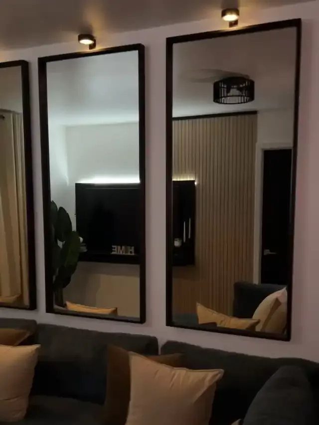 Three matching rectangular mirrors with black frames hanging above a grey couch.