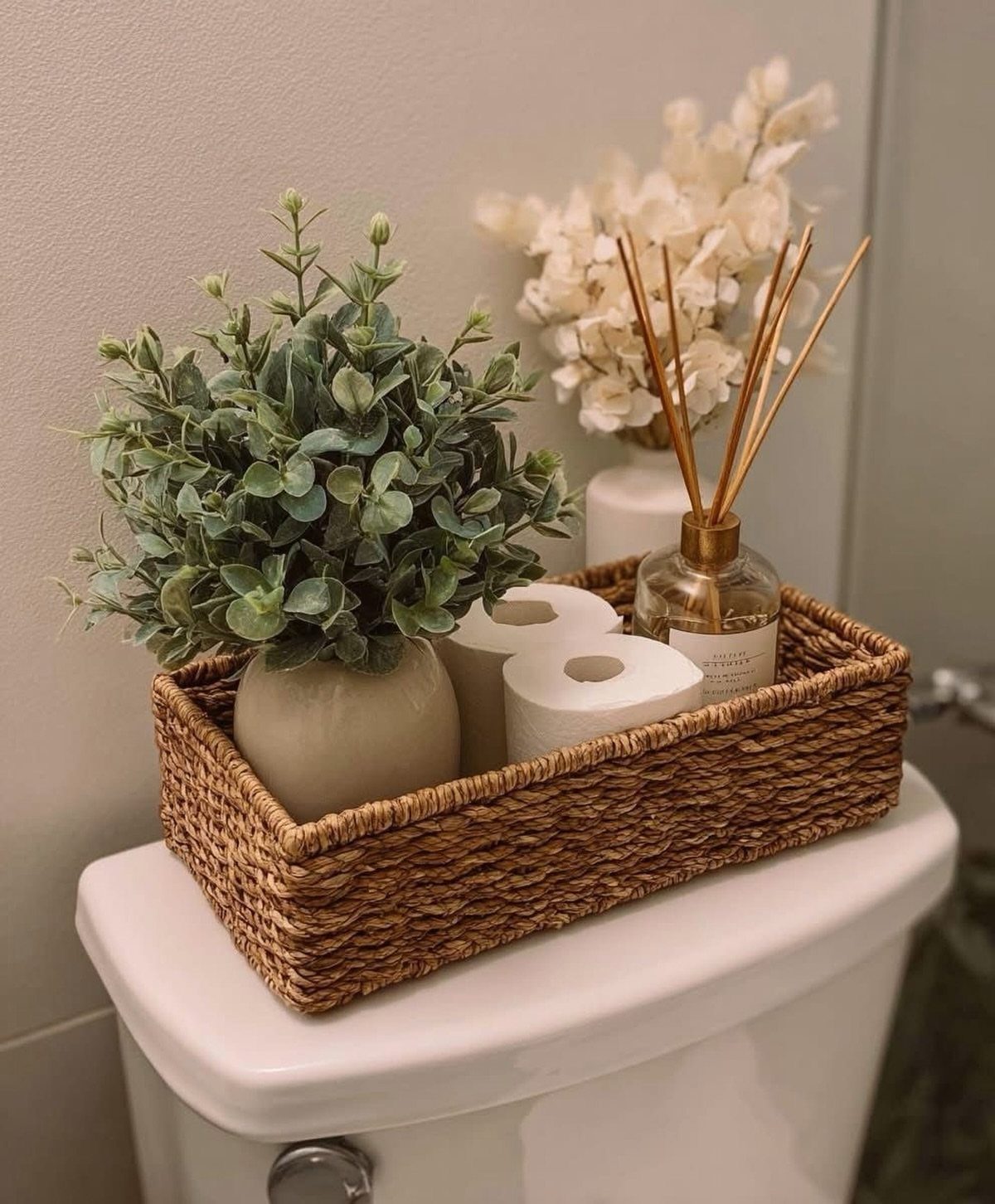 Woven wicker basket on a toilet tank containing a plant and toilet paper.