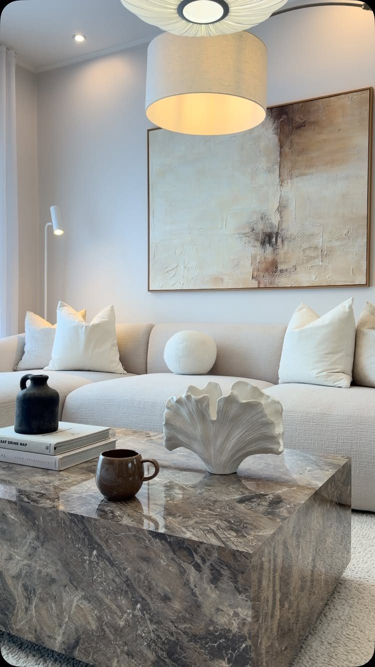 Modern living room with white sofa, marble coffee table, and large abstract art.