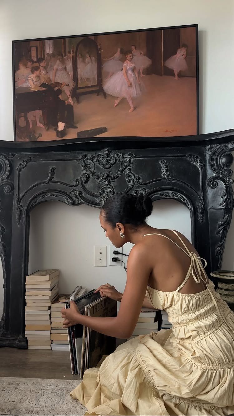 Woman in cream dress by ornate black fireplace with ballerina painting above