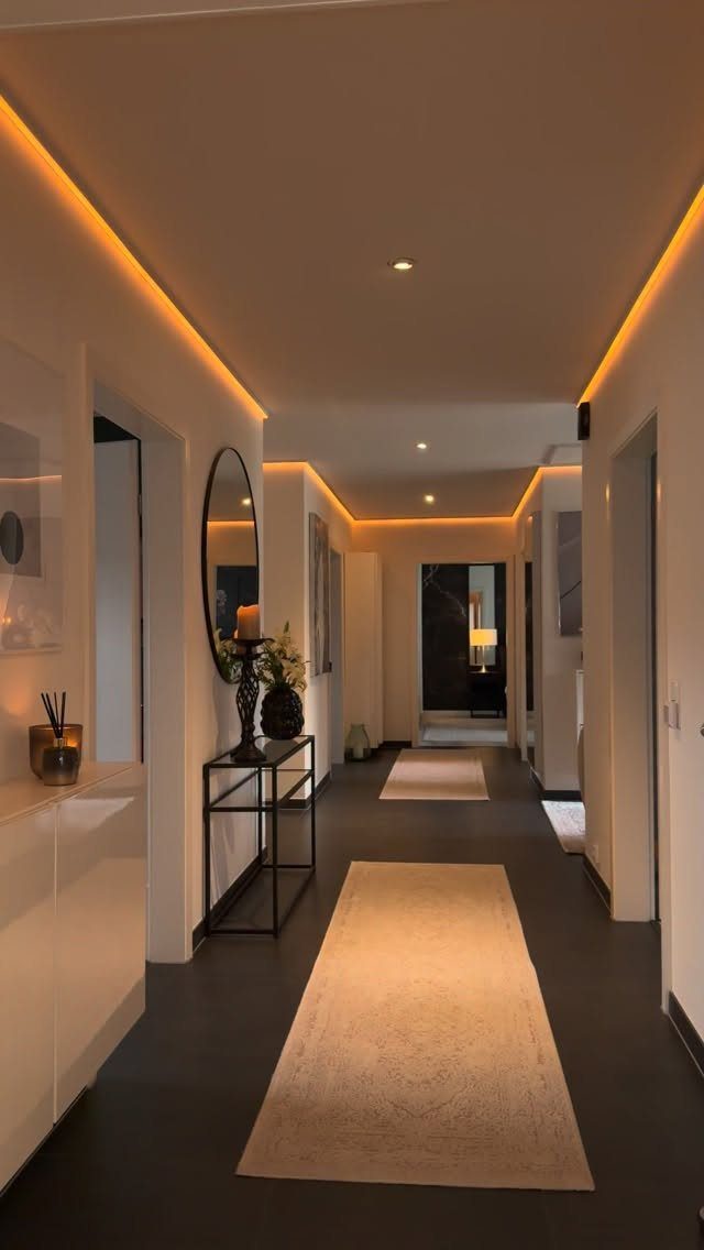 Modern minimalist hallway with warm recessed lighting, dark floors, and a neutral runner rug.