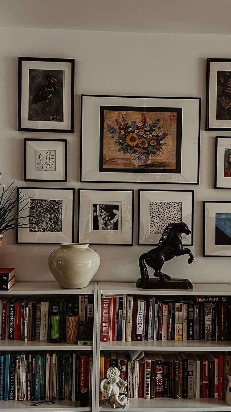 Gallery wall with framed art arranged above a white bookshelf with books and decor.