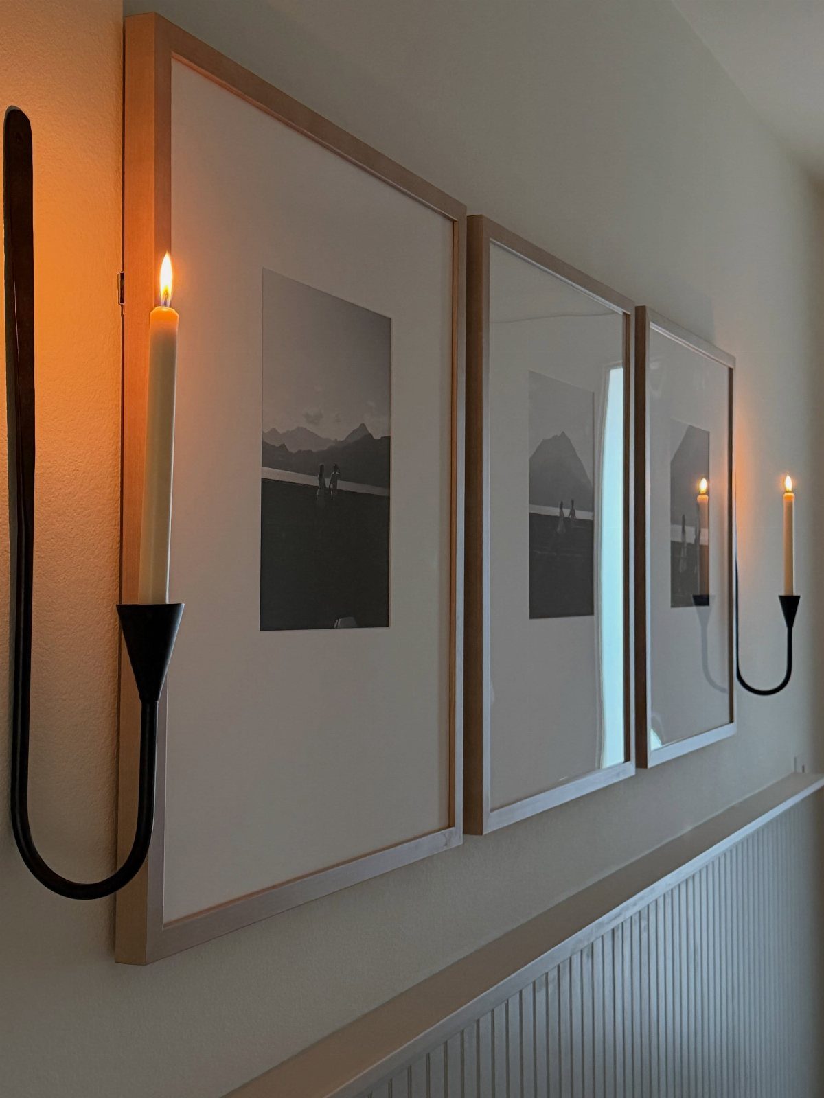 Three framed black and white photos arranged horizontally on a wall with candles.