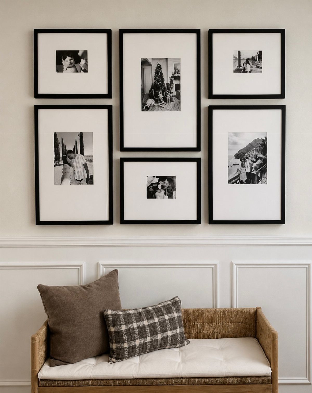 Black-framed black-and-white photos arranged on a wall above a woven couch with pillows.