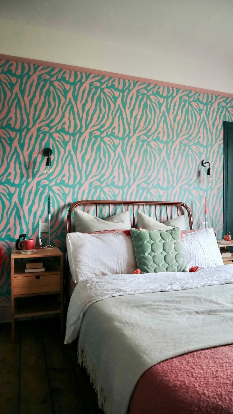 Bedroom wall with pink and green organic patterns behind a bed with linens.