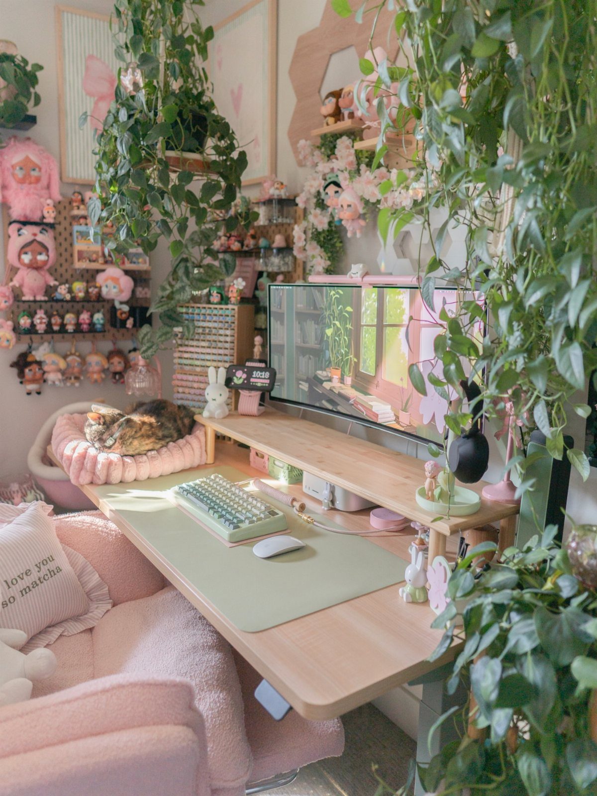 Pink desk setup with a green desk mat and lush trailing green plants.