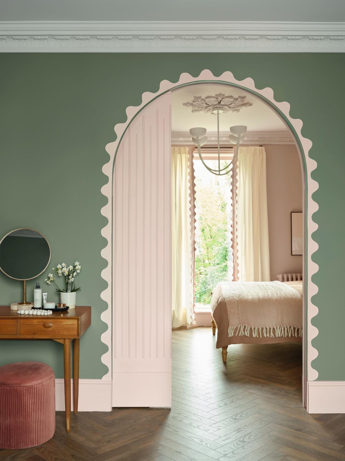 Sage green room with a scalloped pink archway leading to a pink bedroom.