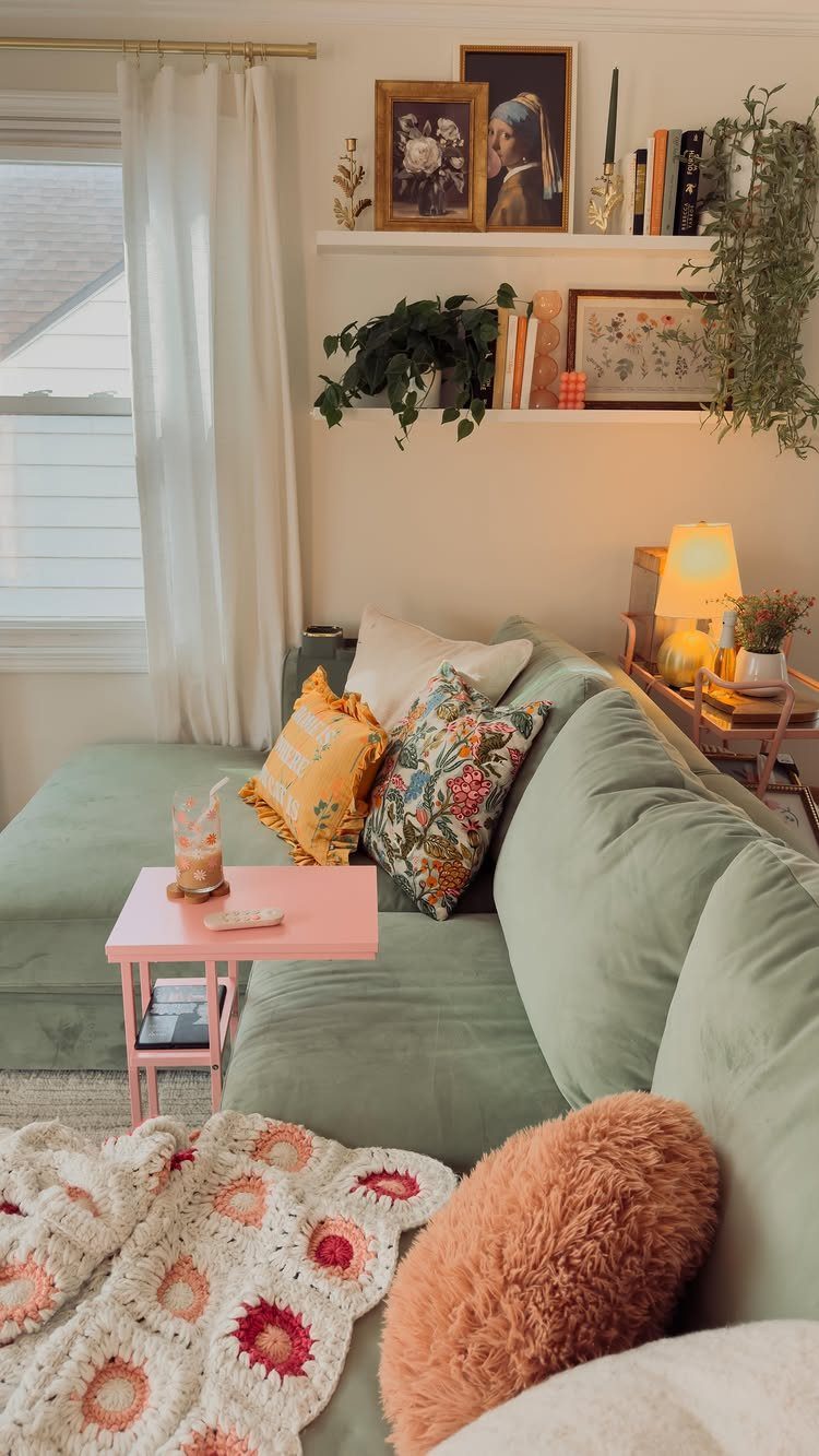 Light green sofa with pink side table and wooden floating shelves on white walls.
