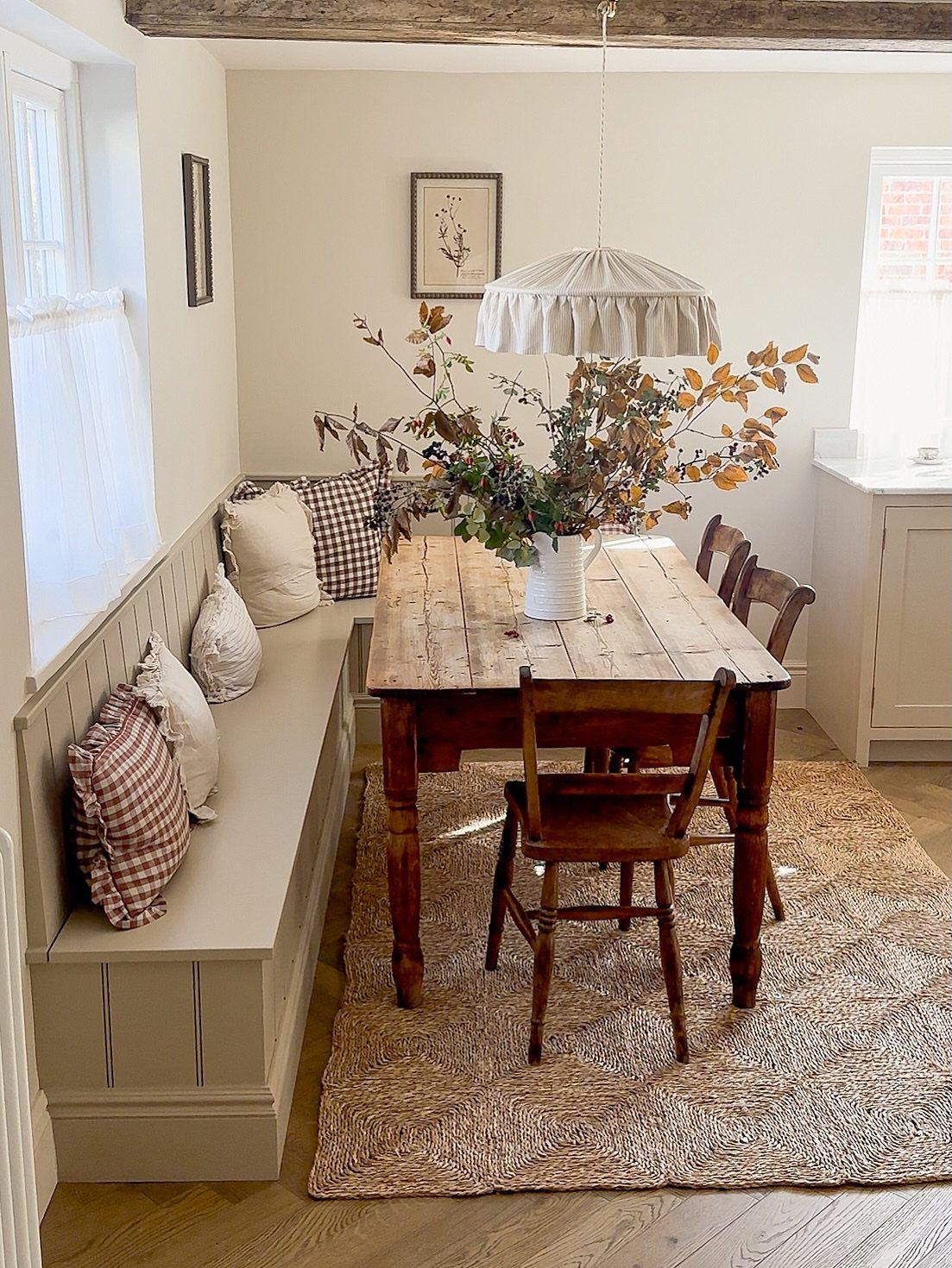 Built-in tan banquette seating with pillows next to a rustic wooden dining table.
