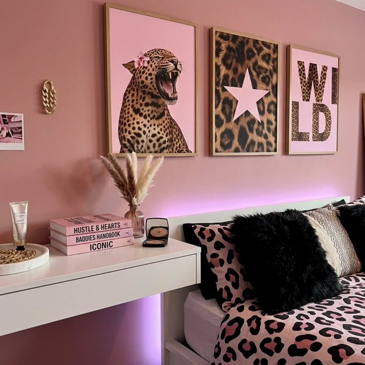 Three leopard-themed framed prints on a pink wall above a white desk and bed.