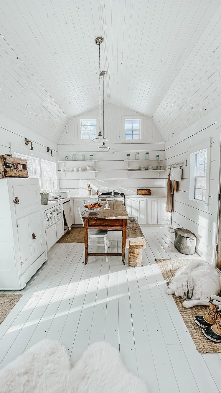 White painted hardwood floors in a bright, rustic white cottage kitchen and dining area.