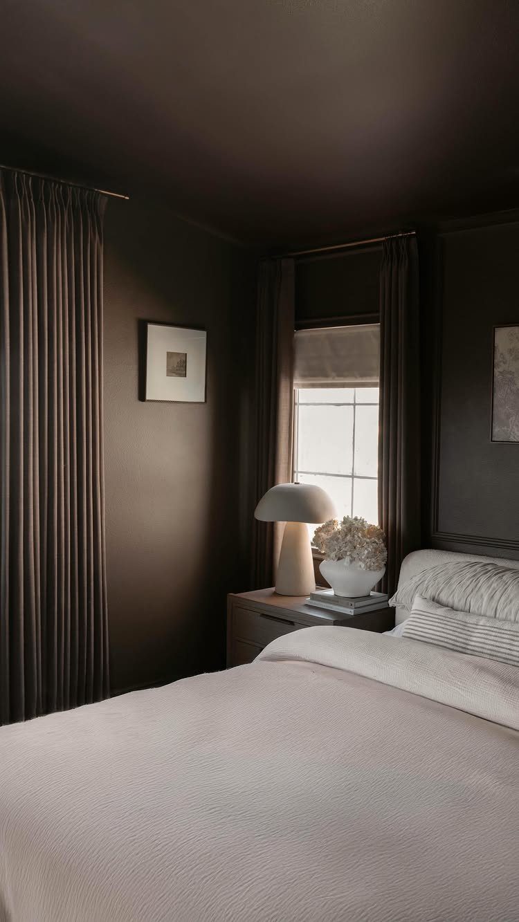 Dark brown curtains and a light roman shade in a moody bedroom