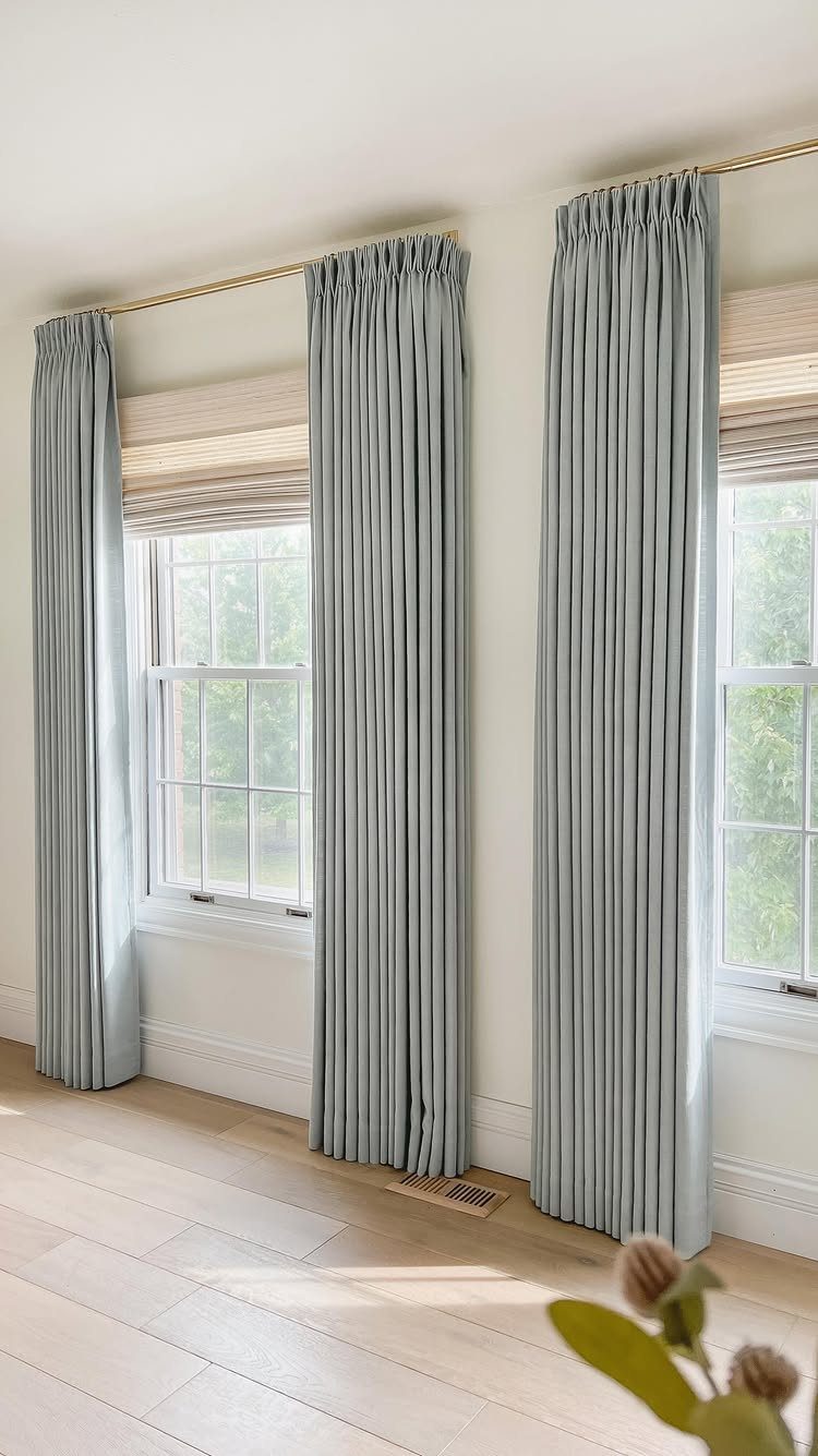 Light blue curtains and beige roman shades on two white-walled windows.