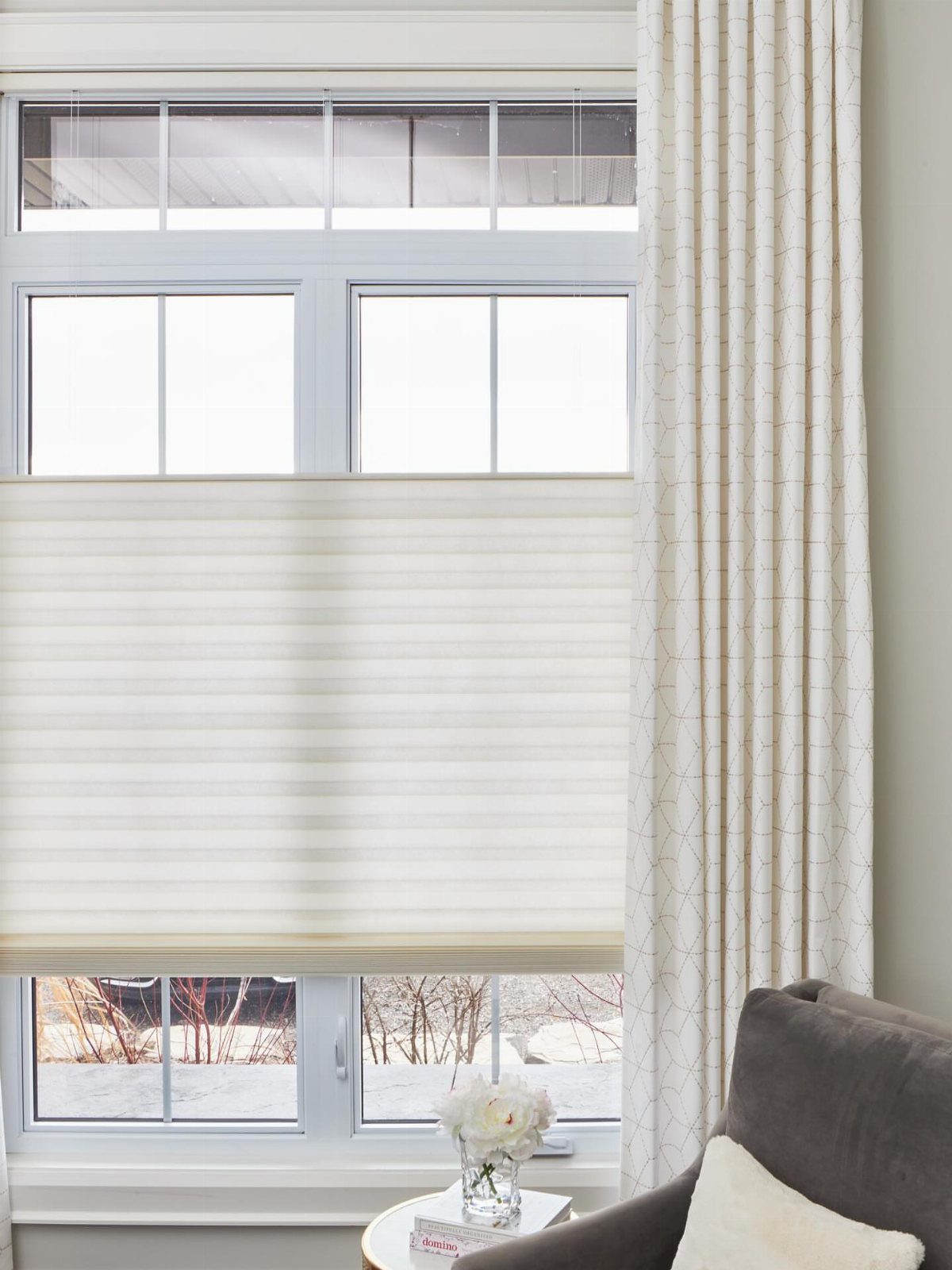 White roman shade and patterned curtains framing a window in a bright room.