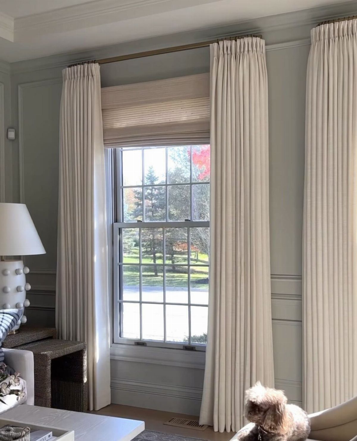 White roman shades and matching curtains framing a window in a grey room.