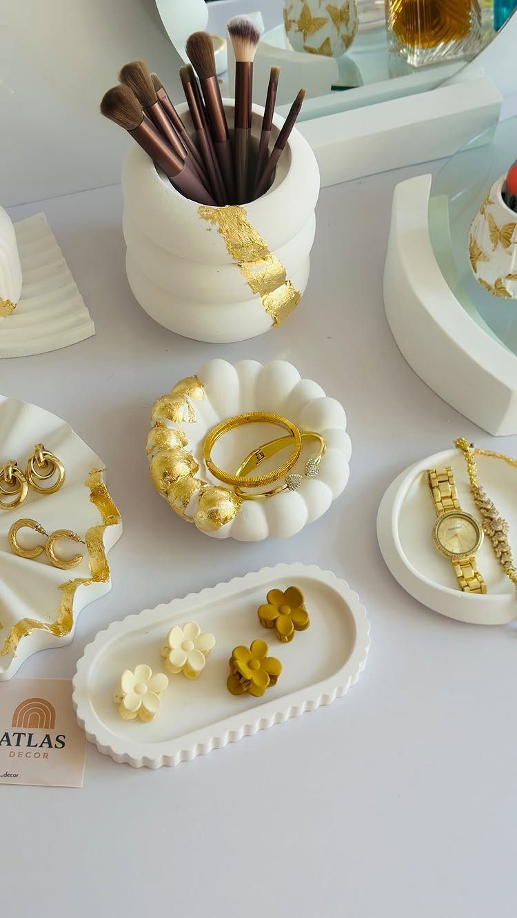 White clay jewelry trays with gold accents holding rings, a watch, and necklaces.