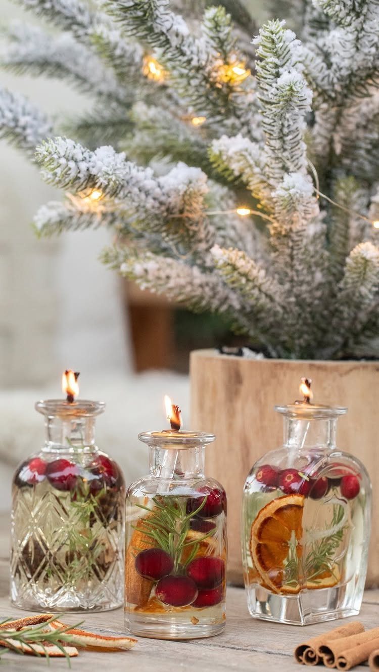 Three glass jars with floating candles, cranberries, and orange slices near snowy branches.