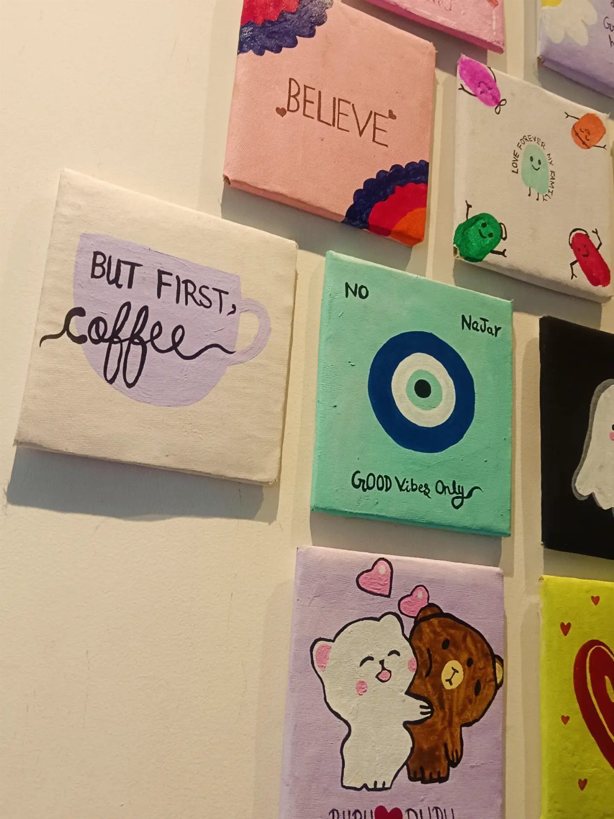 Small square canvas paintings with colorful art and quotes hanging on a wall.