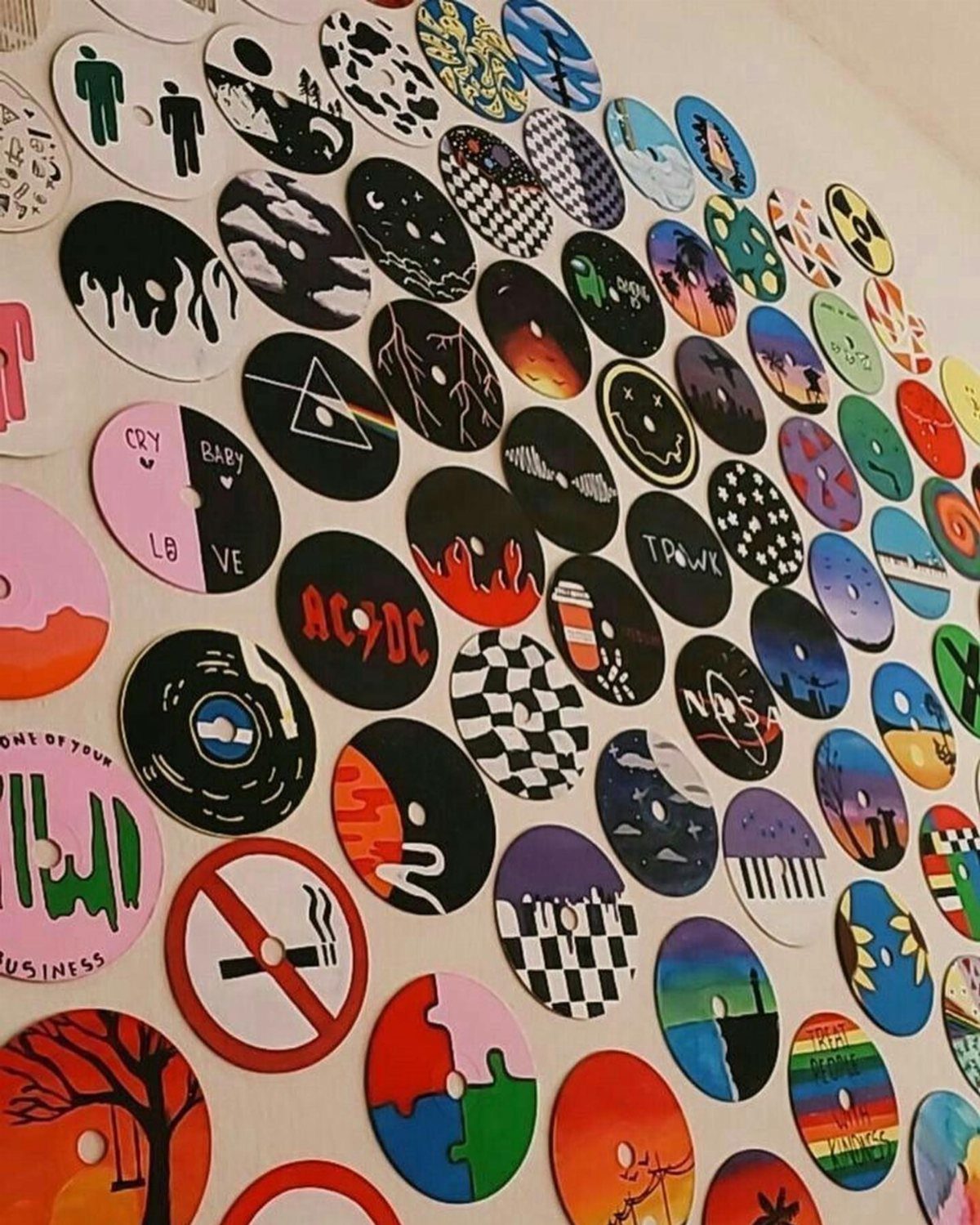 Painted compact discs with various colorful designs arranged as wall decor on white wall