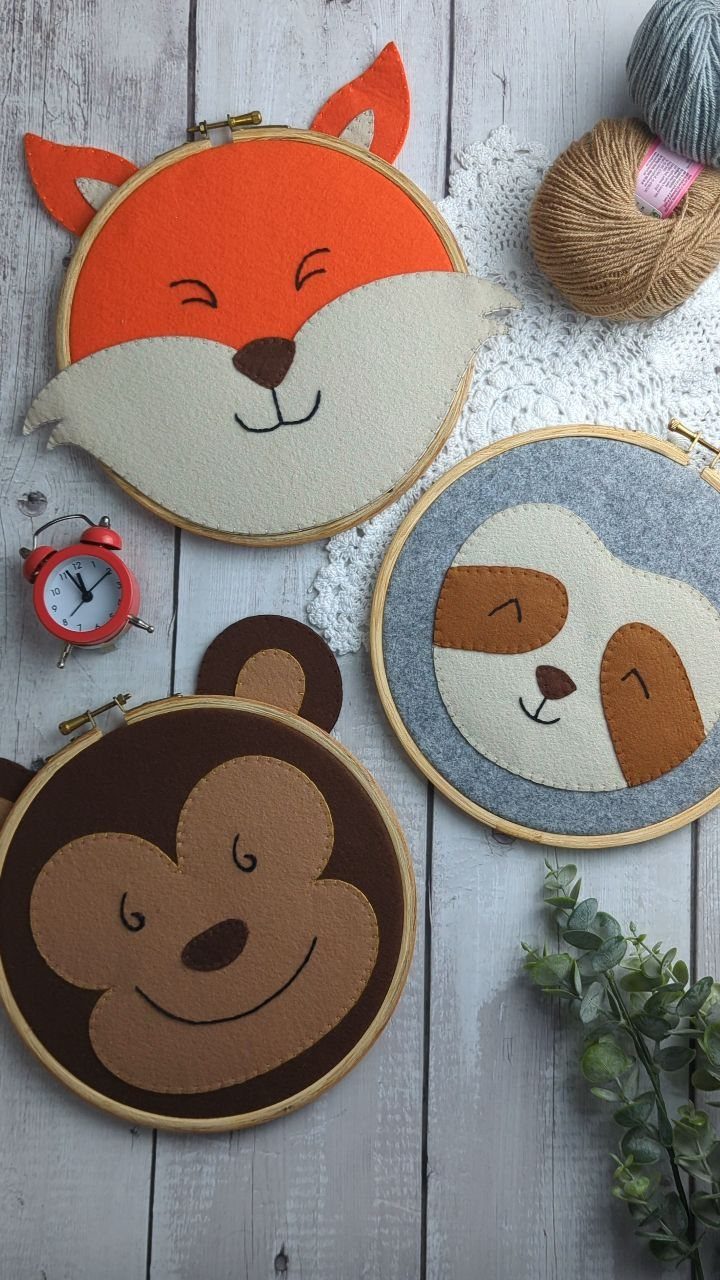 Three felt animal faces in embroidery hoops on a grey wooden background.