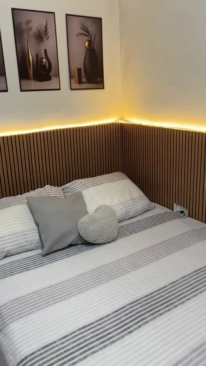 Wooden slat headboard with warm LED lighting behind a bed with striped bedding.