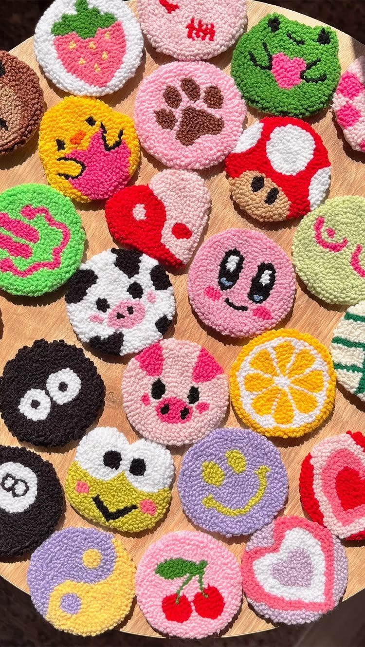 Colorful punch needle coasters with cute fruit and animal designs on wooden table.