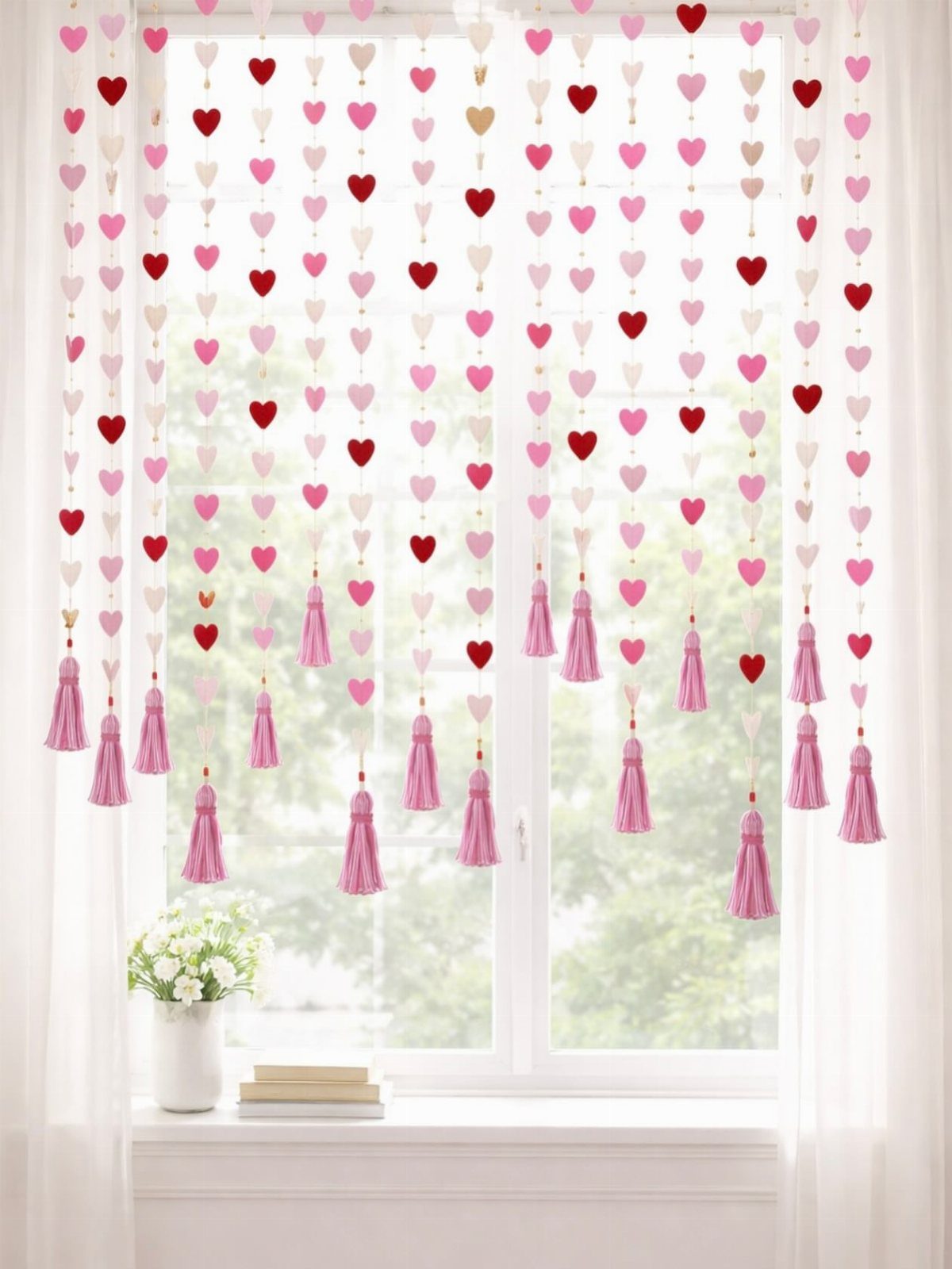 Heart garlands with pink yarn tassels hanging in front of a bright window