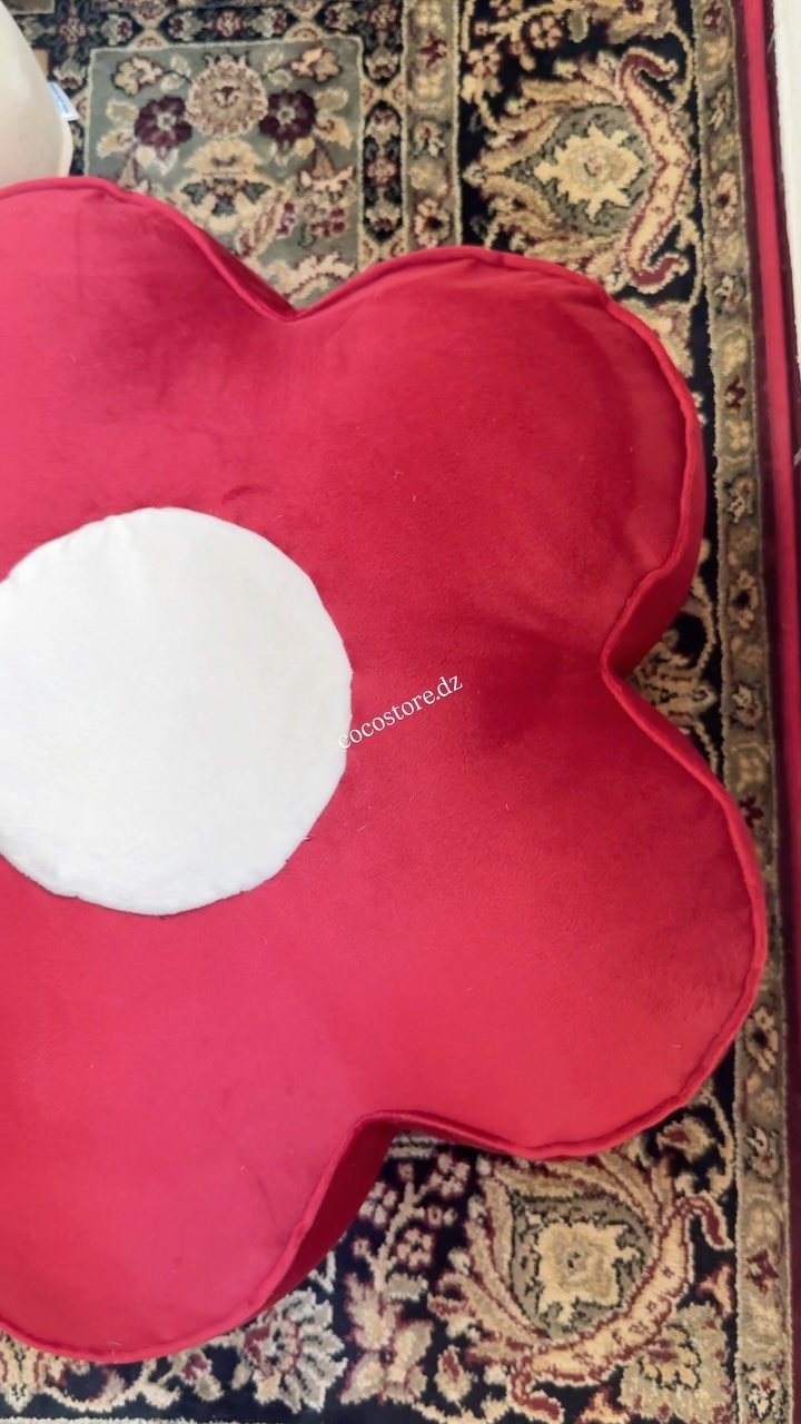 Red flower-shaped pillow with a white center on a patterned oriental rug.