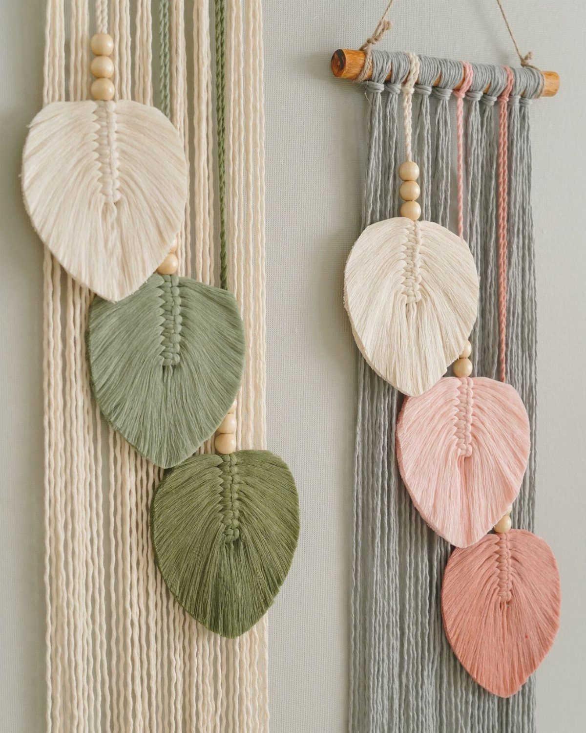 Macrame wall hangings with knotted textile leaves in cream, green, and pink tones.