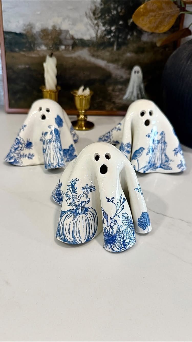 Three white ceramic ghost figurines with blue floral patterns on a white surface.