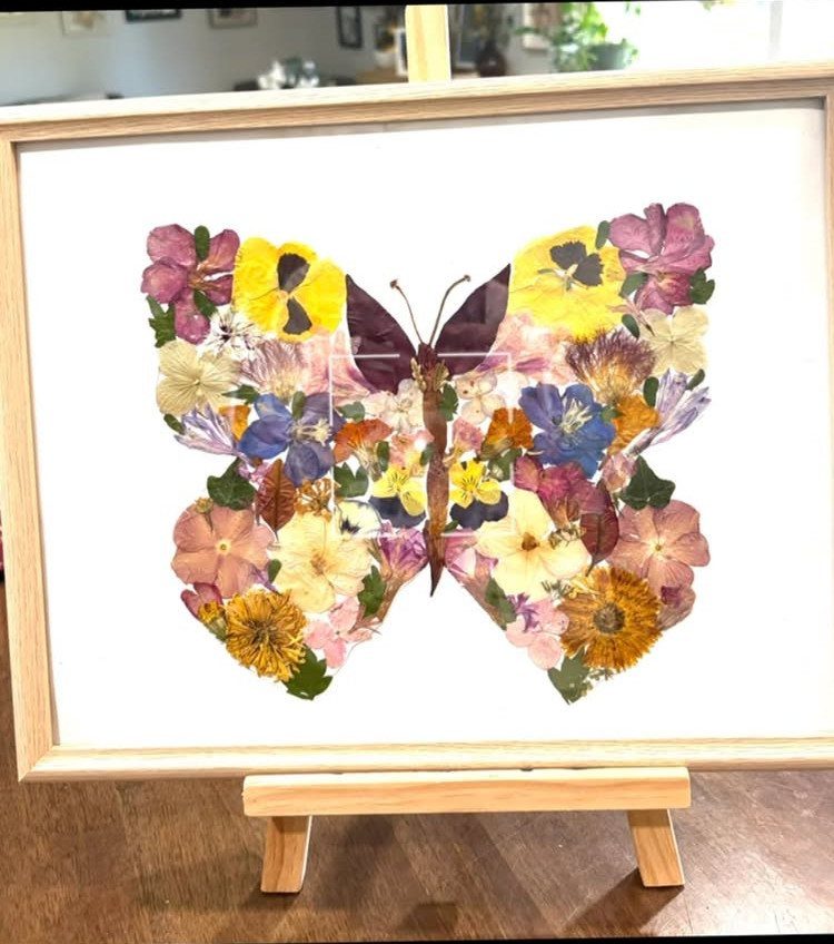 Butterfly shape made of colorful pressed flowers inside a light wood frame on easel