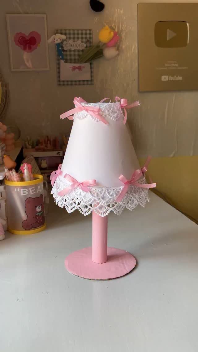 Handmade lamp with pink base and white shade decorated with lace and bows.