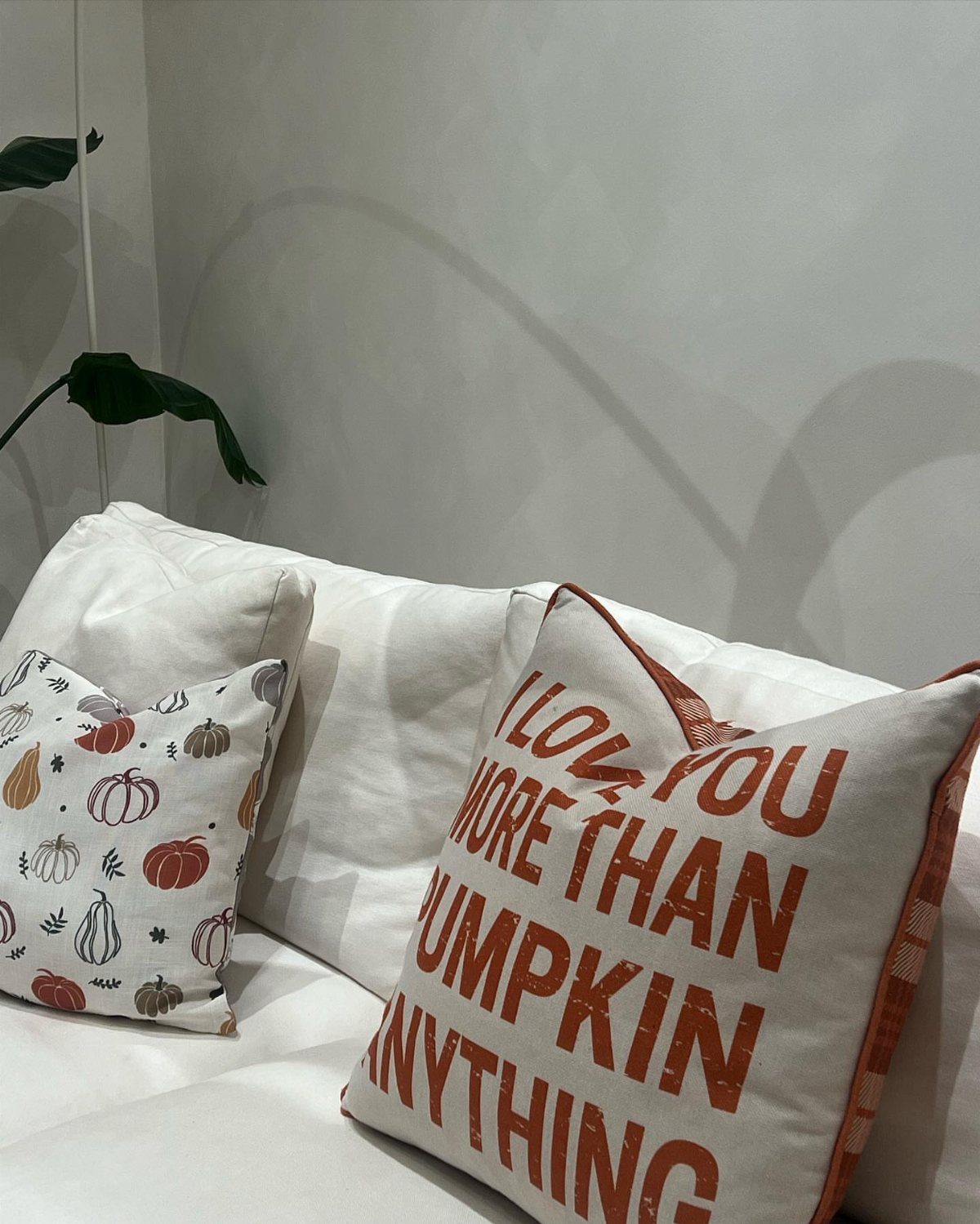 White throw pillows with pumpkin patterns and orange text on a white couch.