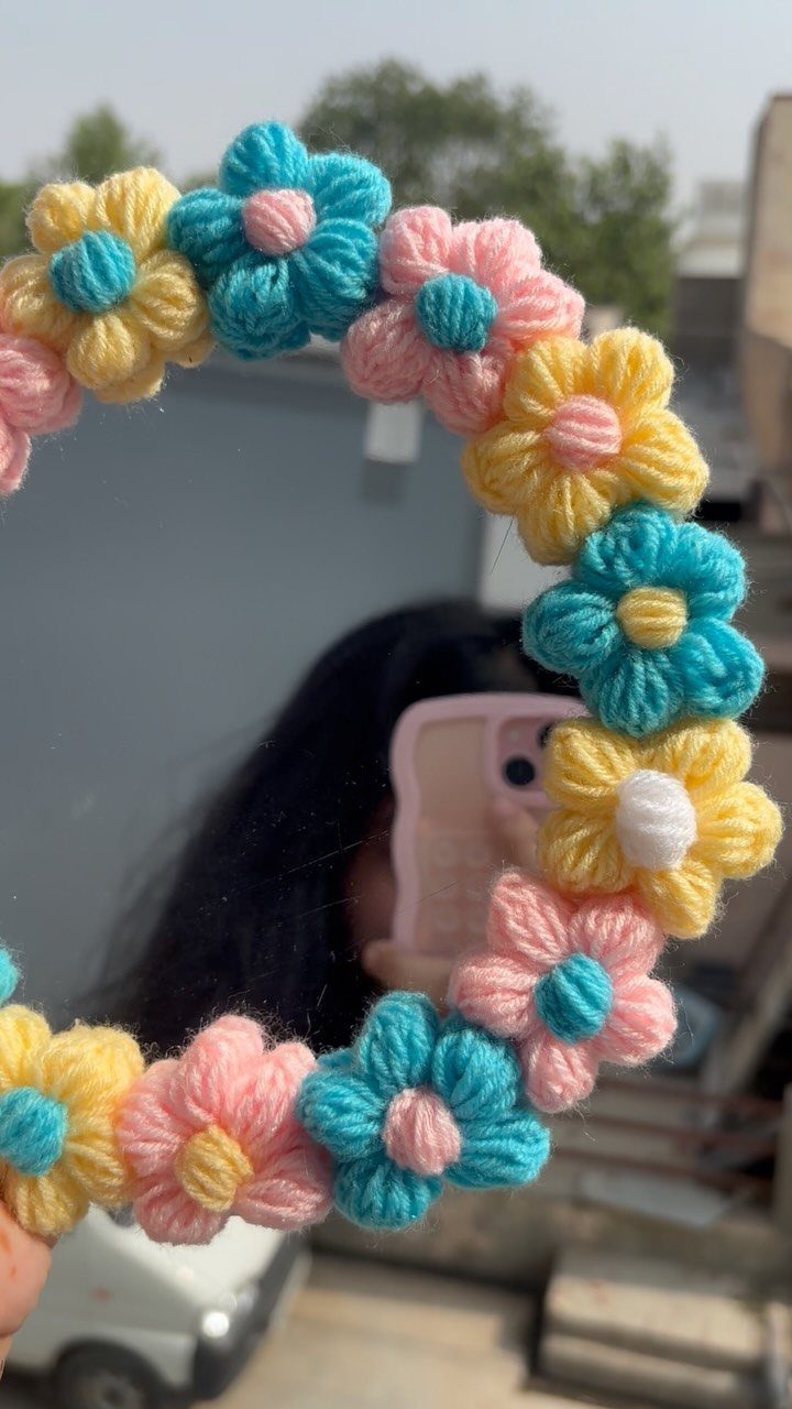 Round mirror framed with colorful crochet flowers held by a person taking a selfie.